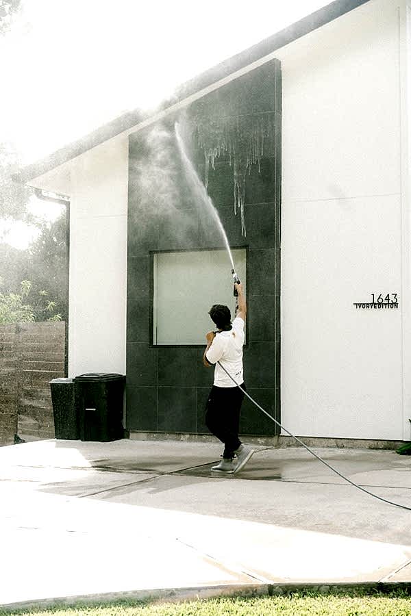 Pressure washing exterior siding on a modern white Houston home