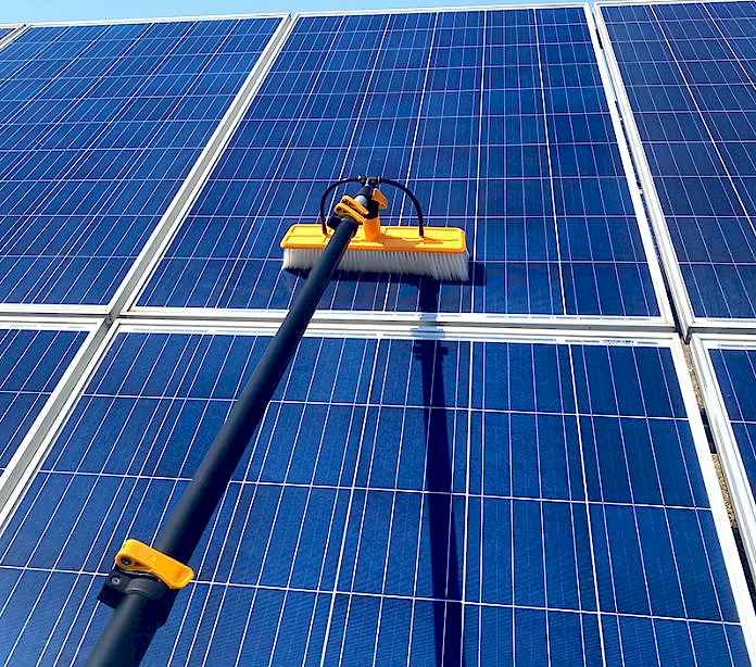Technician using a soft-bristle brush to clean a residential solar panel array