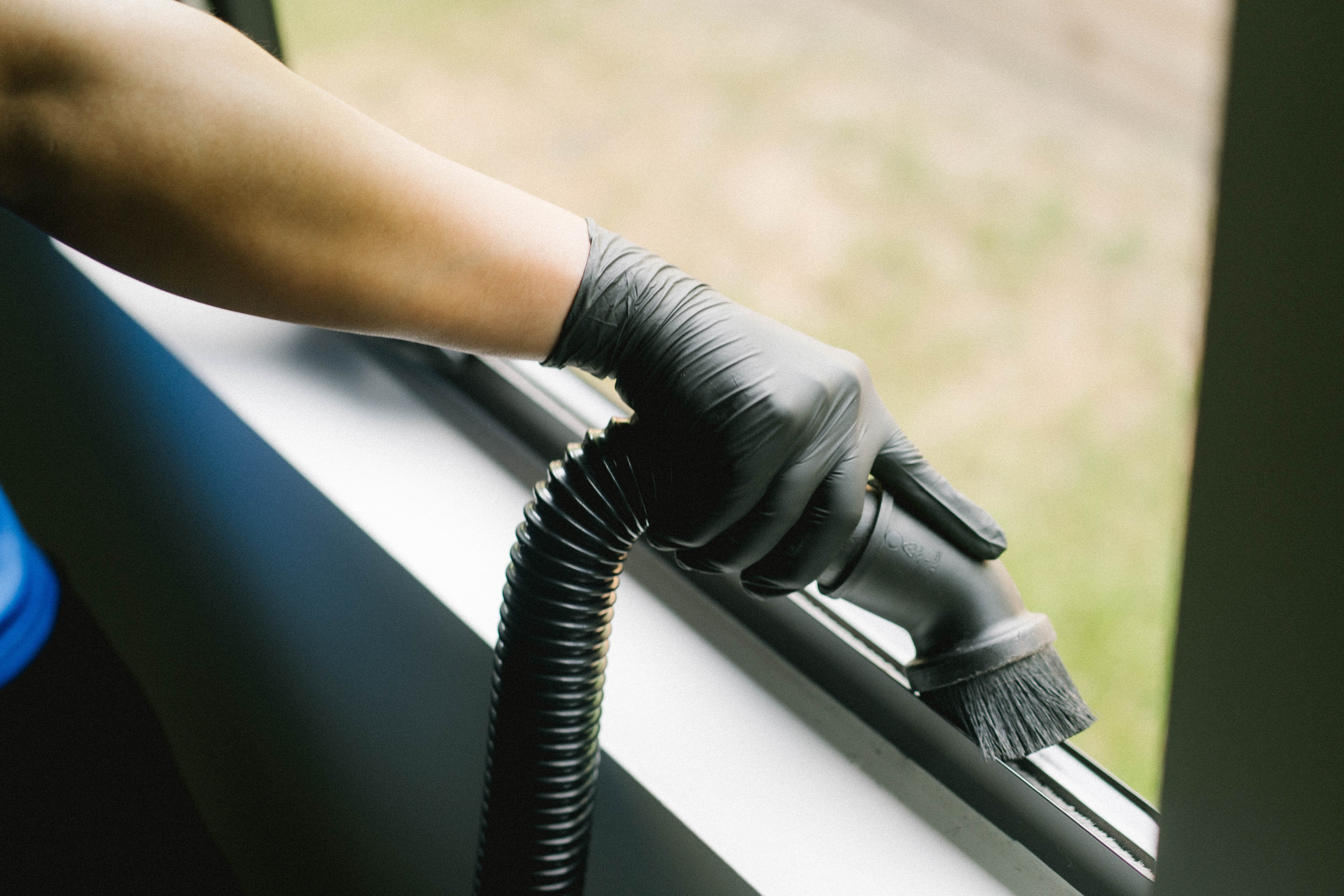 Technician hand-detailing a window track with a brush and vacuum tool